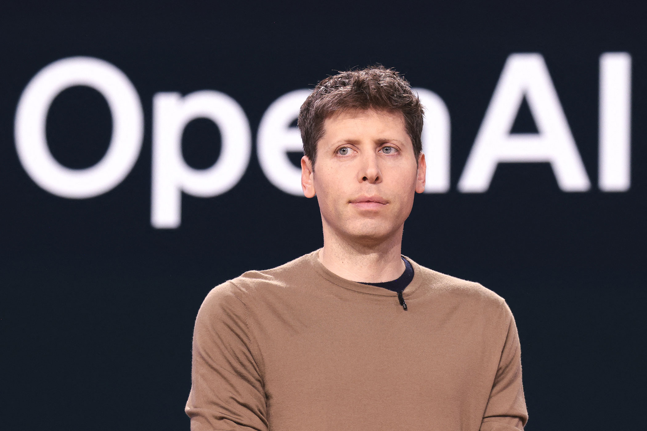 ภาพระยะใกล้ของ Sam Altman หน้าโลโก้ OpenAI สื่อถึงการชี้แจงต่อสาธารณะ